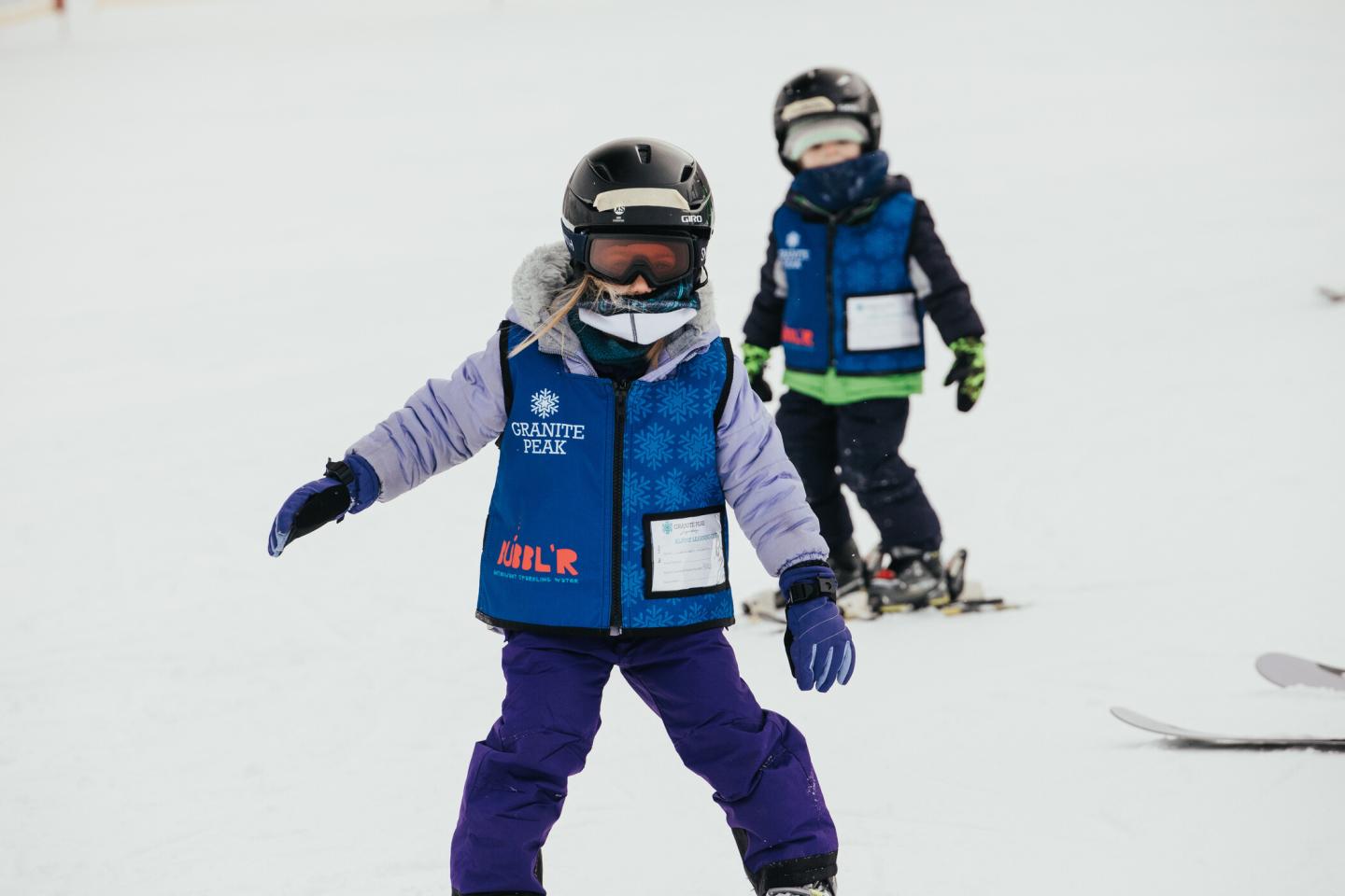 Two kids skiing in lesson jackets