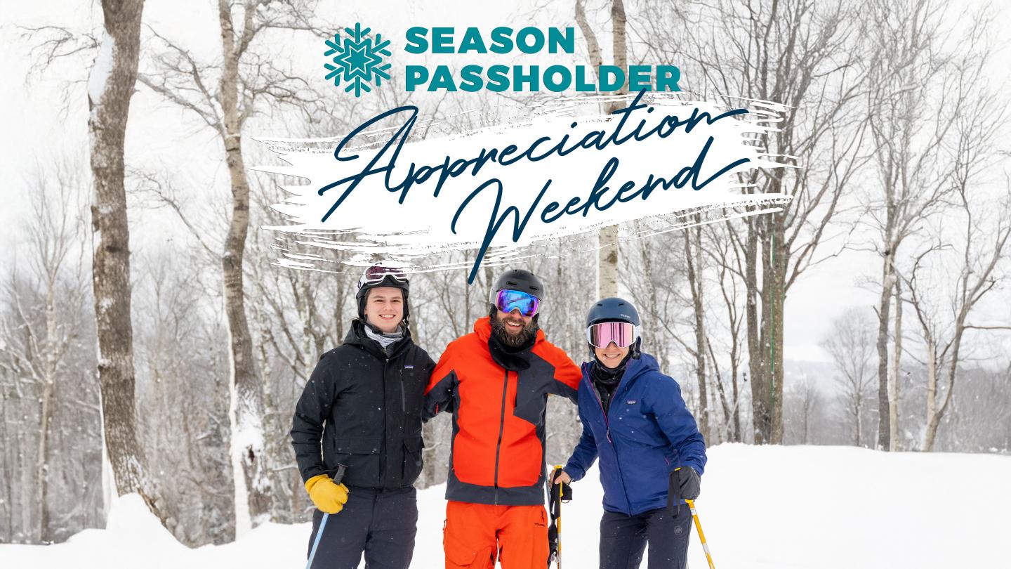 Three people in winter gear smiling on a snowy landscape with bare trees.