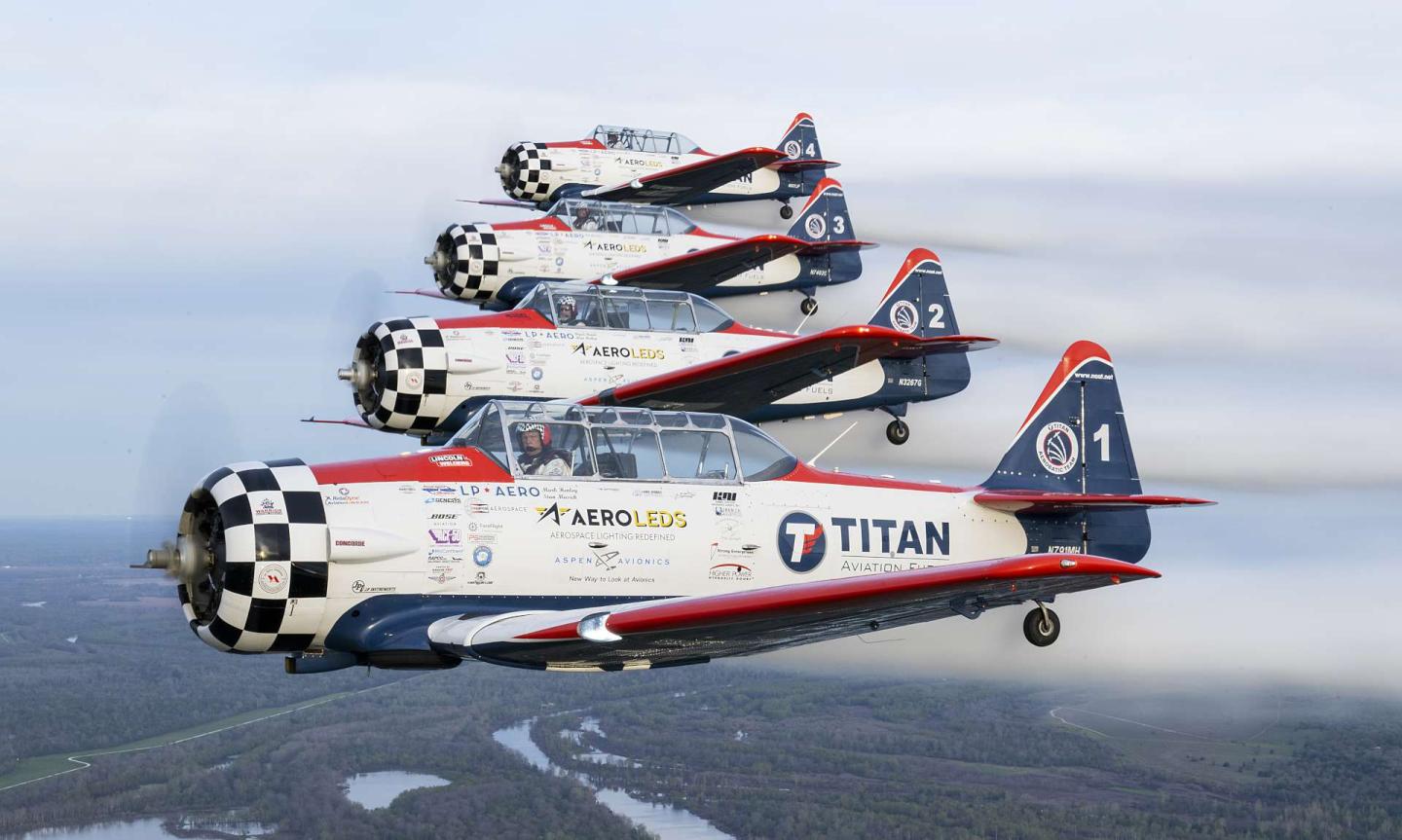 Four vintage planes flying in formation over a landscape.