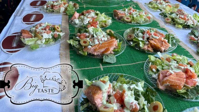 Salads with salmon, olives, and lettuce on a table with a decorative logo.