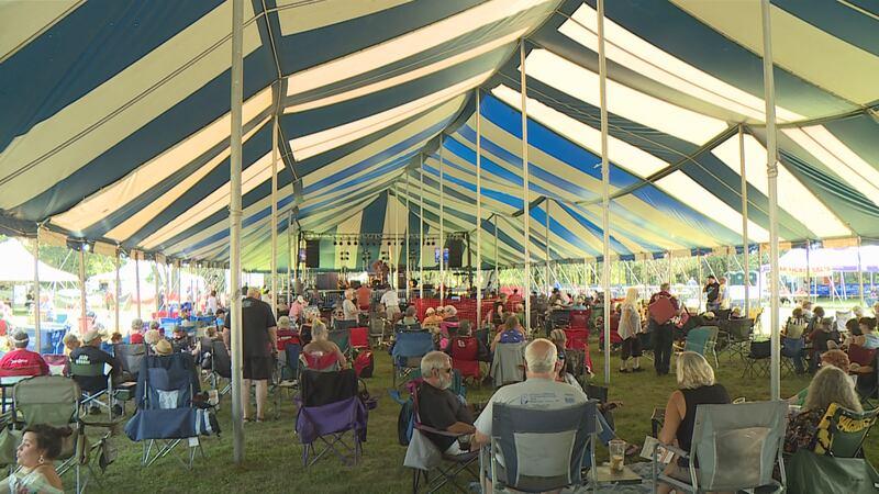 Festival attendees seated under a striped tent enjoying an event.