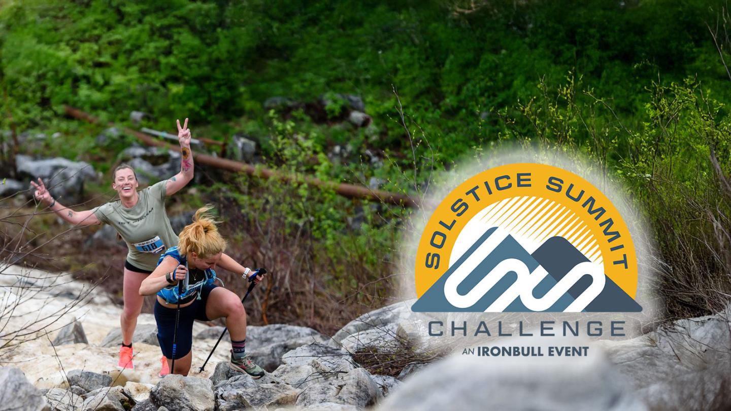 Two women hiking on a rocky trail, one cheering enthusiastically. Logo reads "Solstice Summit Challenge."