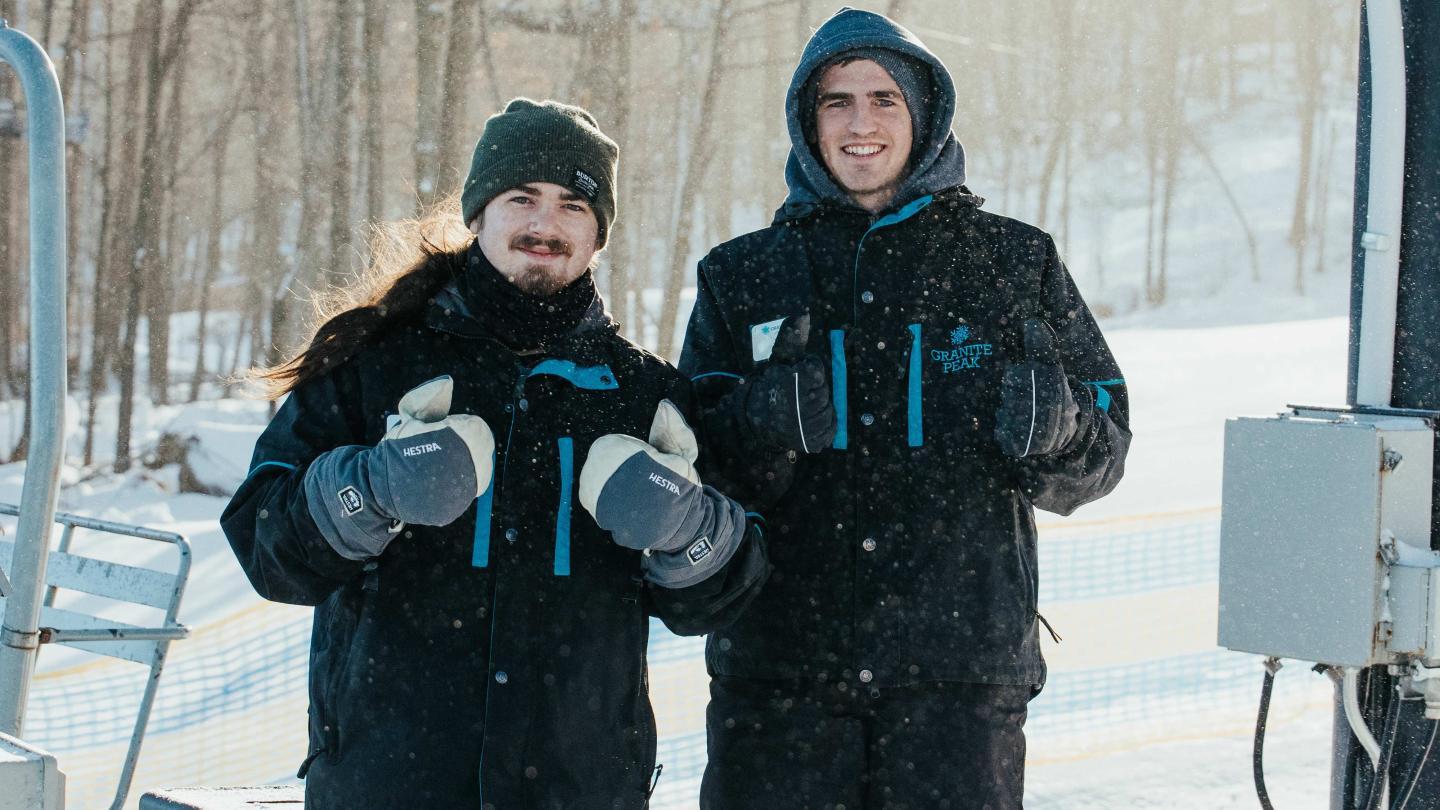 Two people in winter clothing smiling in a snowy outdoor setting.