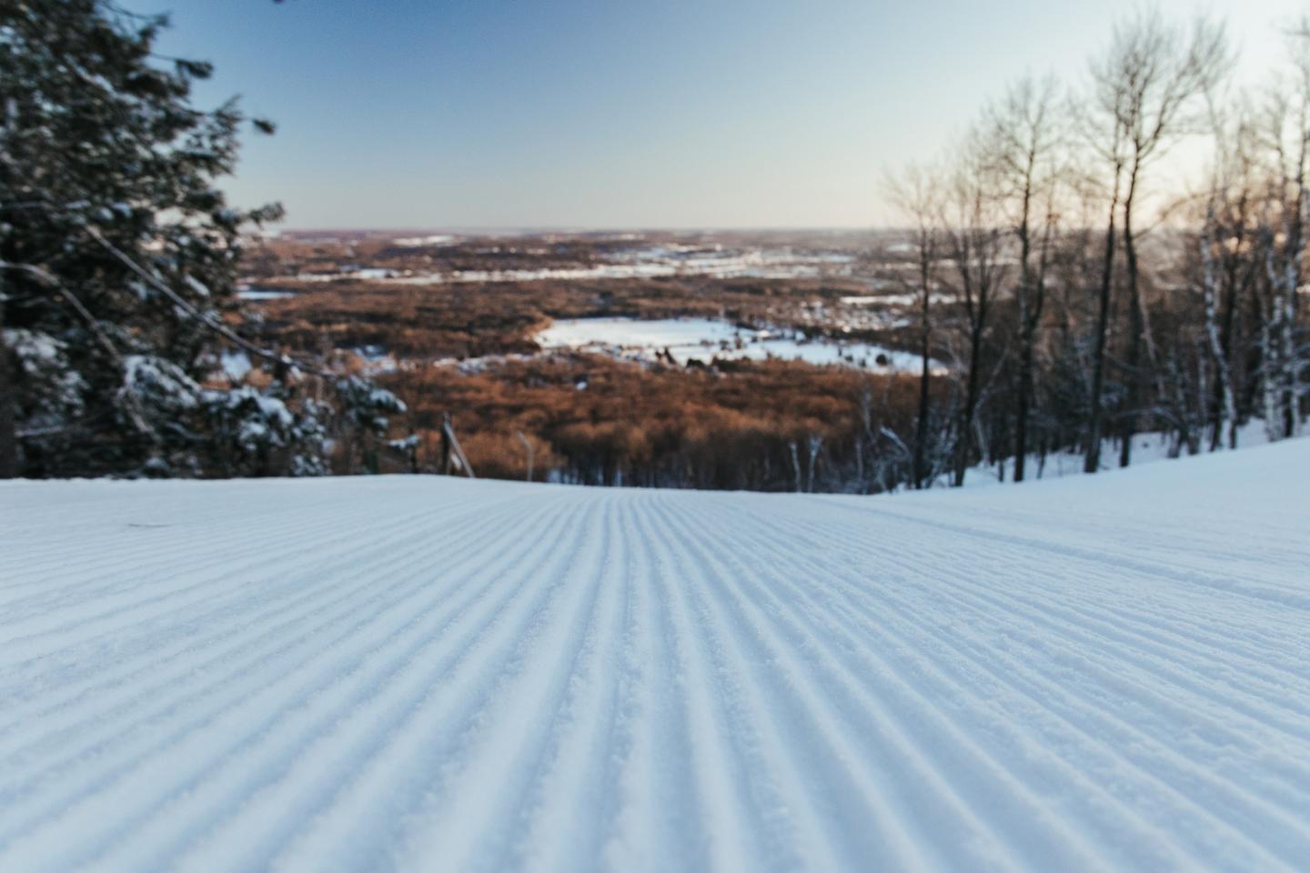 Groomed ski slope overlooking a snowy, wooded valley.
