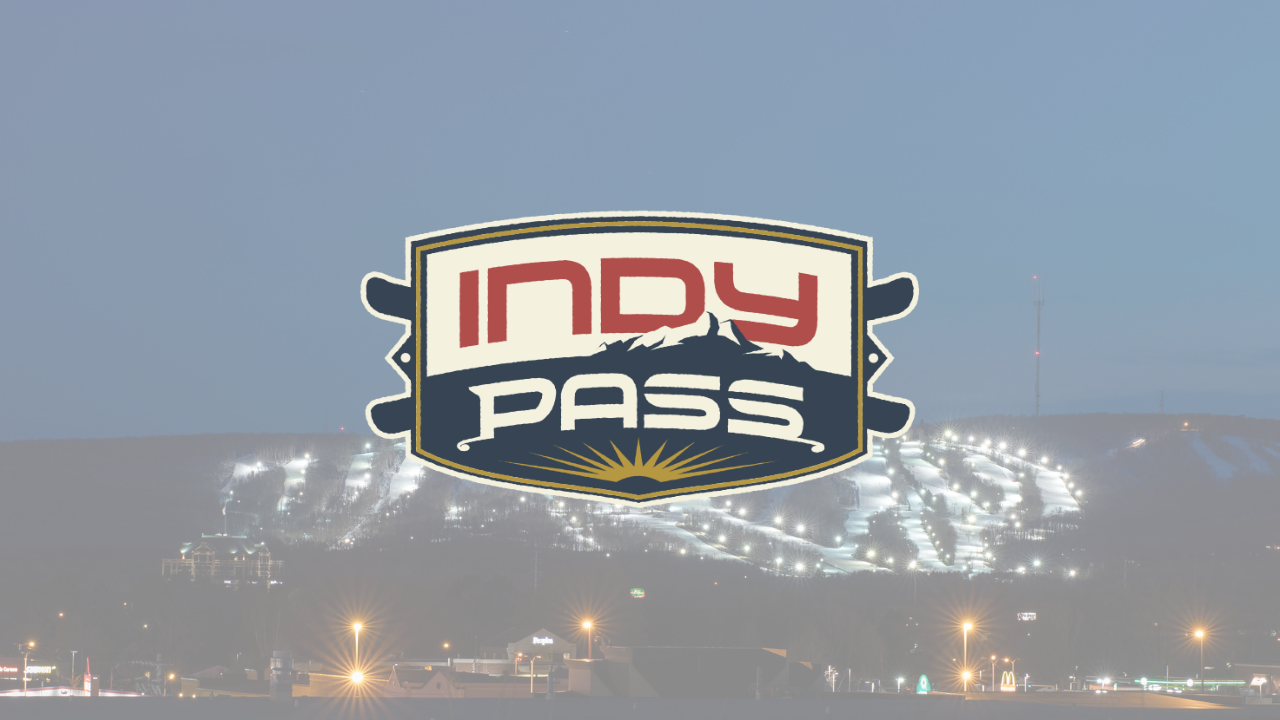 Indy Pass logo over a lit-up ski mountain at dusk.