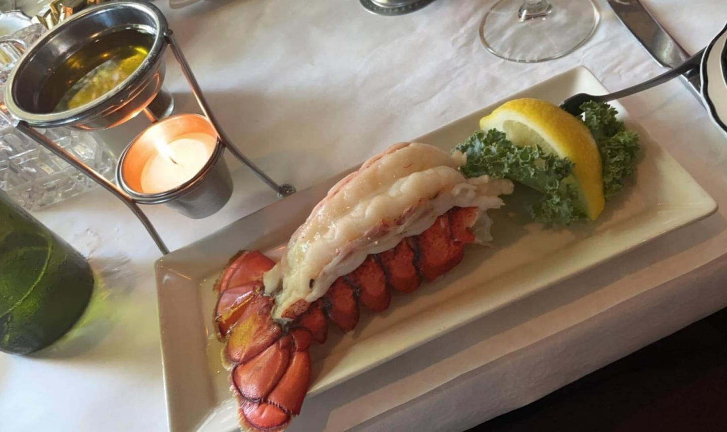 Lobster tail with lemon and parsley garnish on a white plate.
