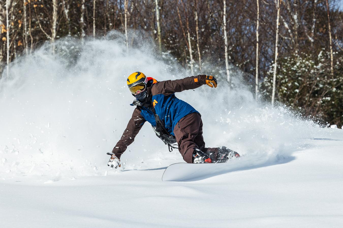 Snowboarder carving through fresh powder on a sunny day.