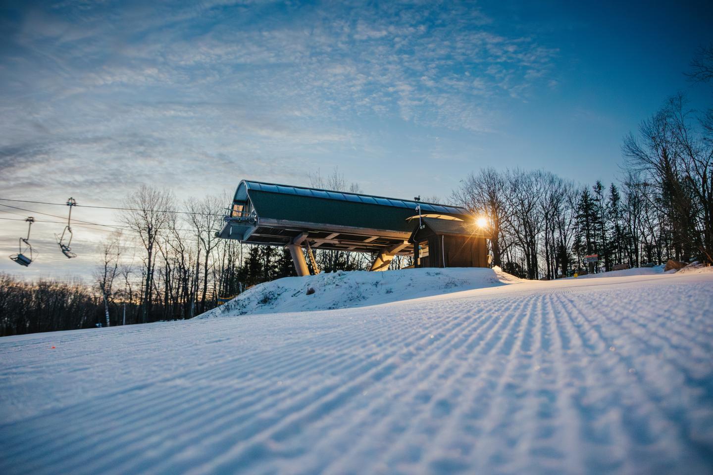 Snowy ski lift at dawn with trees and a clear sky.