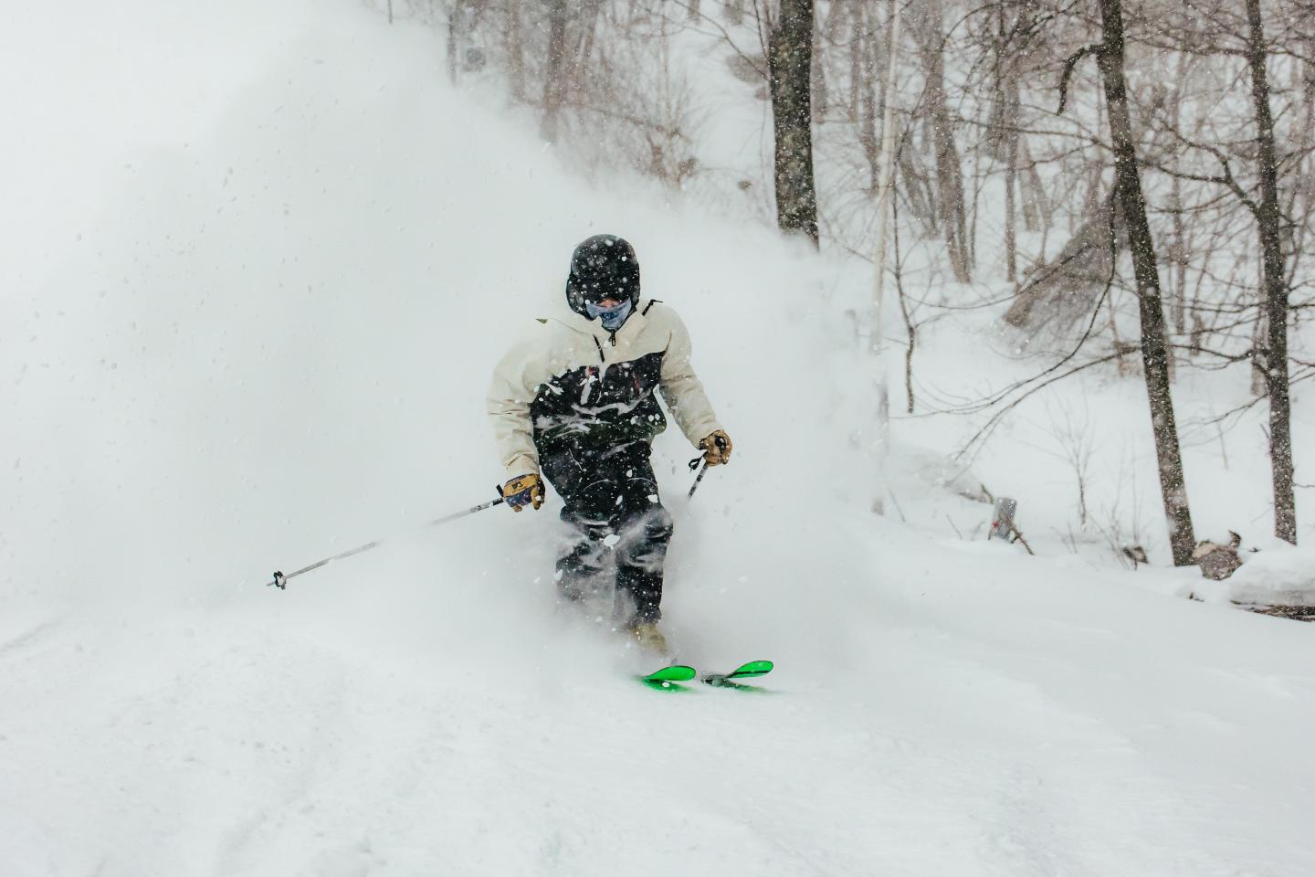 Skier in black and white gear skiing through powder snow in a forest.