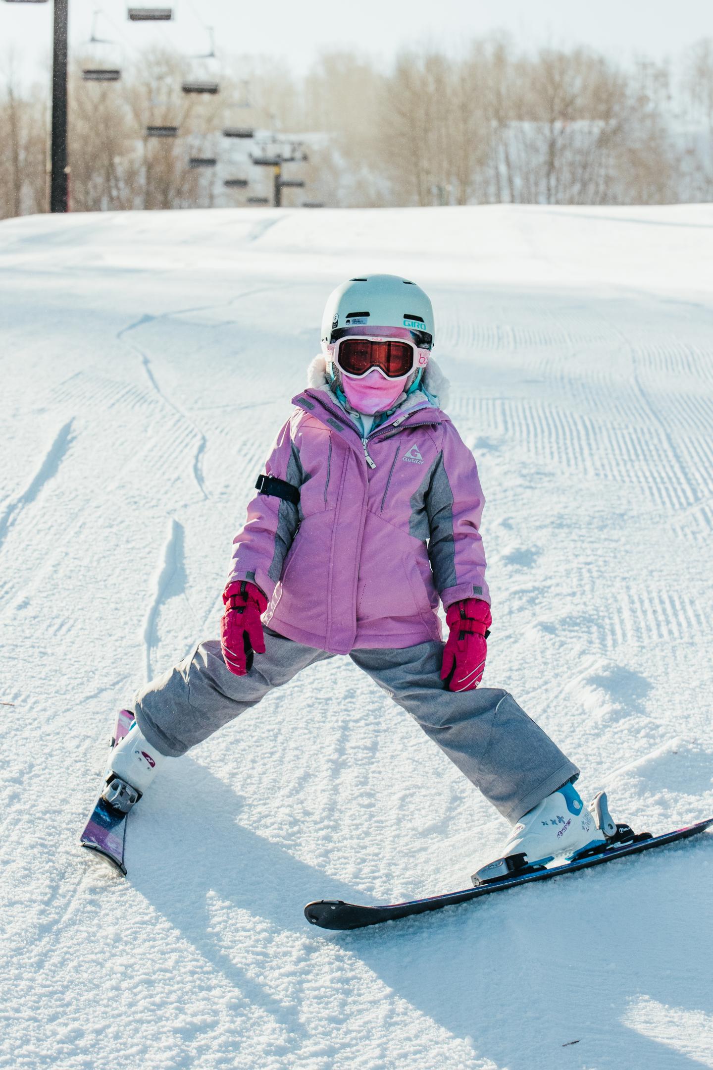 Child skiing in snow, wearing pink jacket and helmet, bright day.