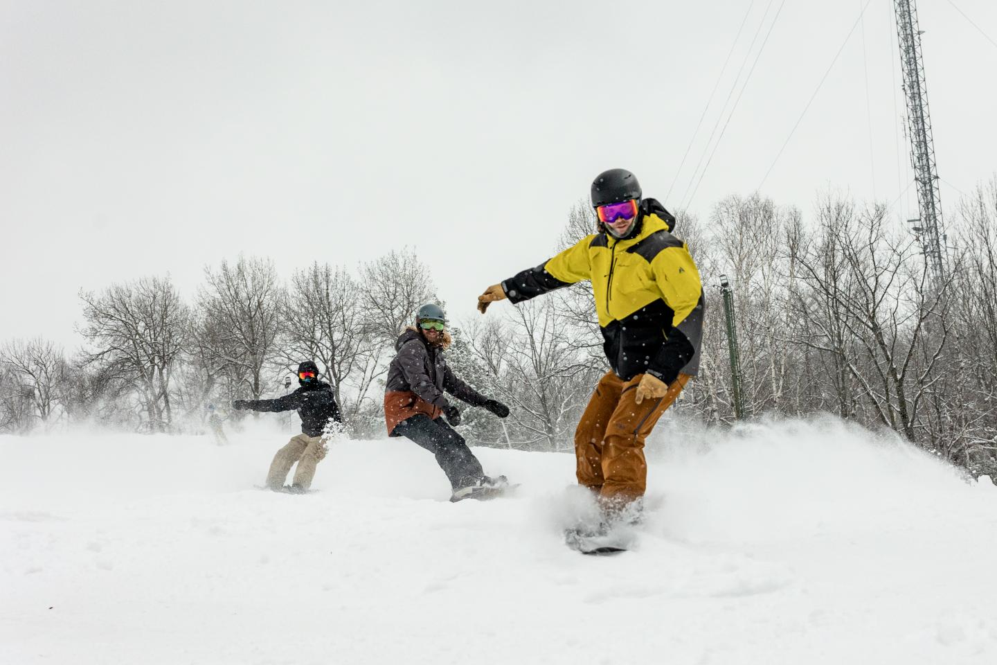 Three snowboarders going downhill in snowy terrain.