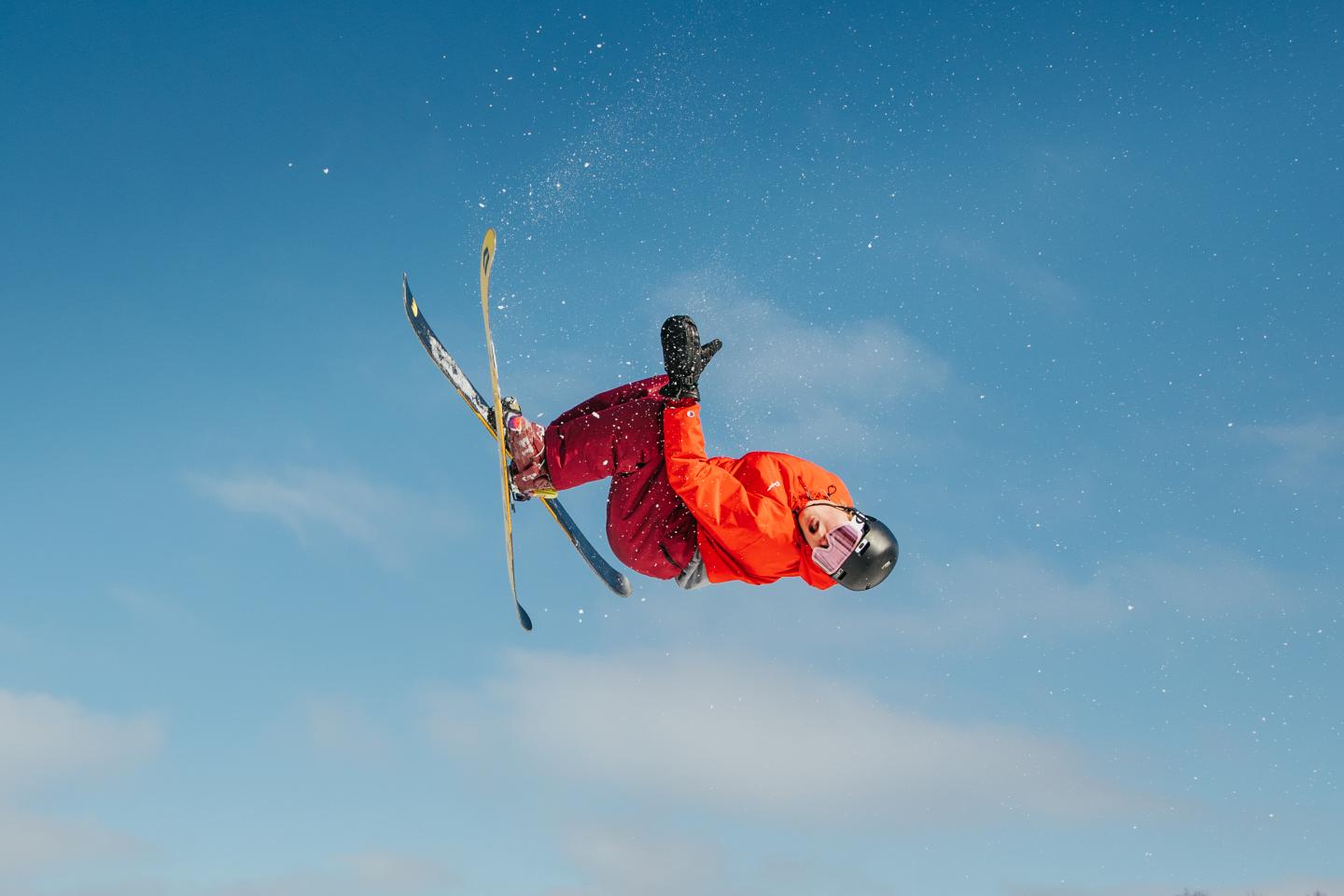 Skier in mid-air backflip against clear blue sky.