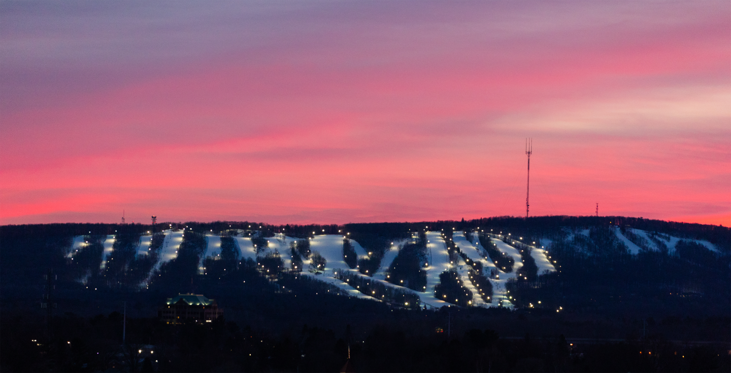 Ski slopes lit up at sunset with a vibrant pink and purple sky.