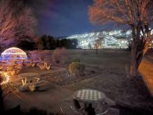 Outdoor seating with glowing dome, night sky, and distant city lights.
