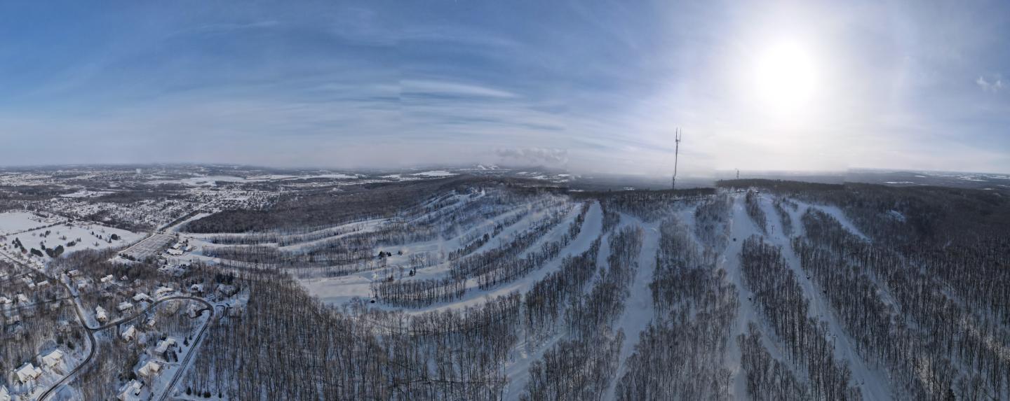 Snowy landscape with ski slopes, trees, and bright sun.