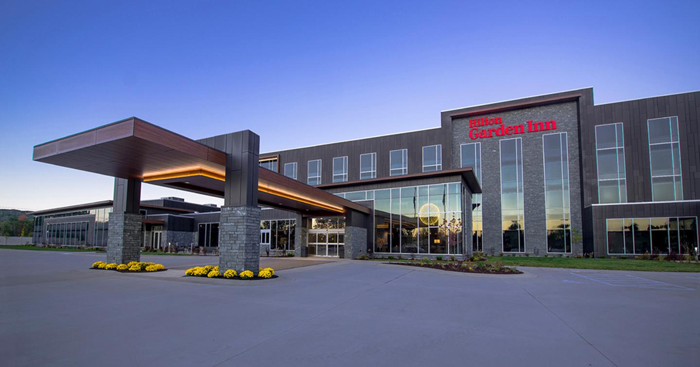 Modern hotel entrance at sunset with a glass facade and canopy.