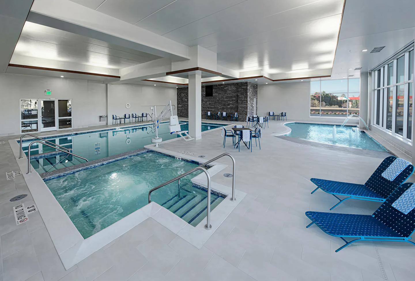 Indoor pool with blue lounge chairs and large windows.