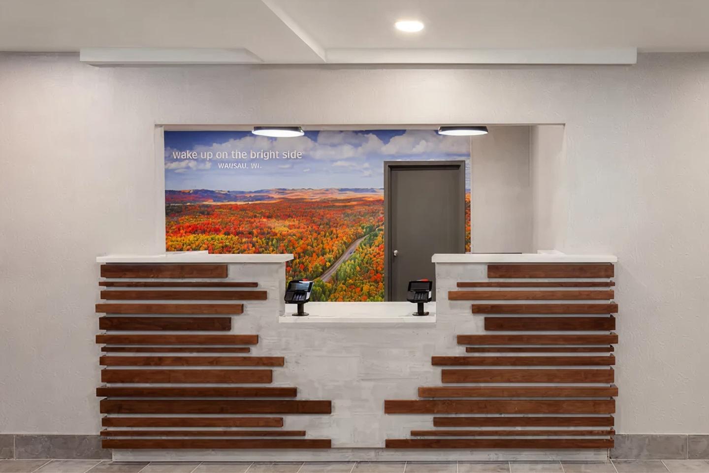 Hotel reception with wooden accents, colorful landscape mural behind.