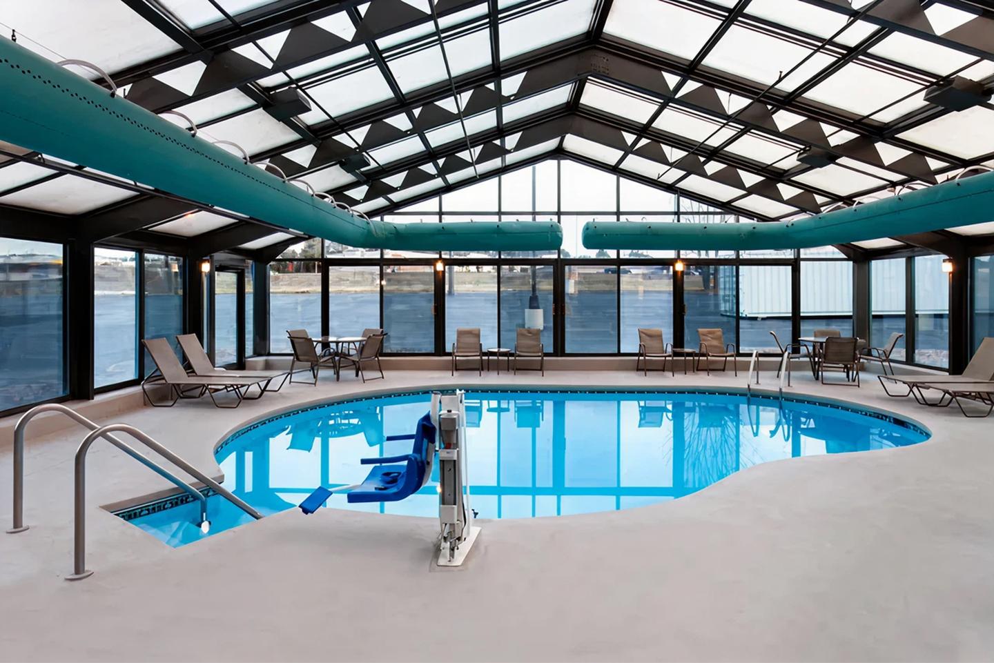 Indoor pool with large windows, blue slide, lounge chairs, and view of a body of water.