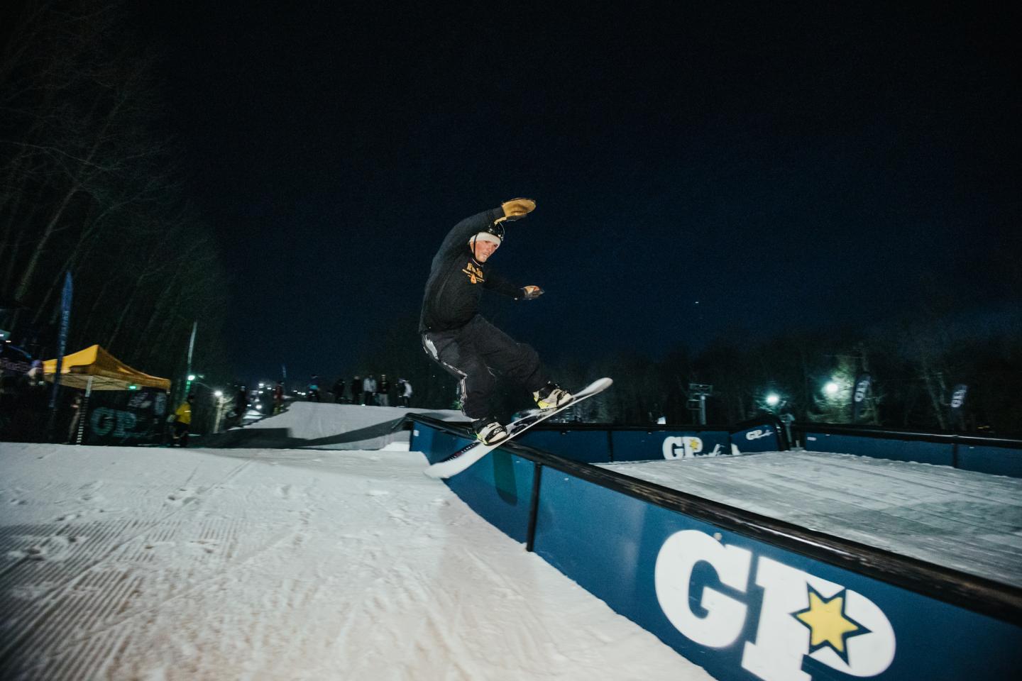 Snowboarder performing a trick on a rail at night.