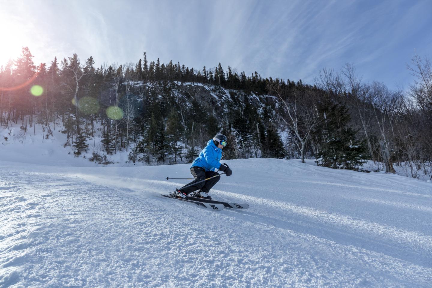 Skier in blue jacket descends a snowy slope under a clear blue sky.