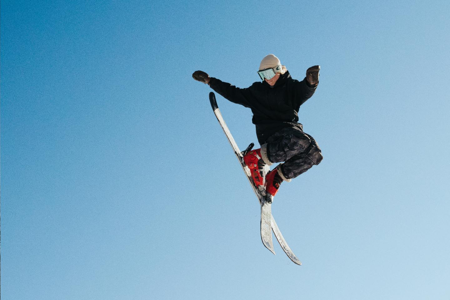 Skier mid-air against clear blue sky.