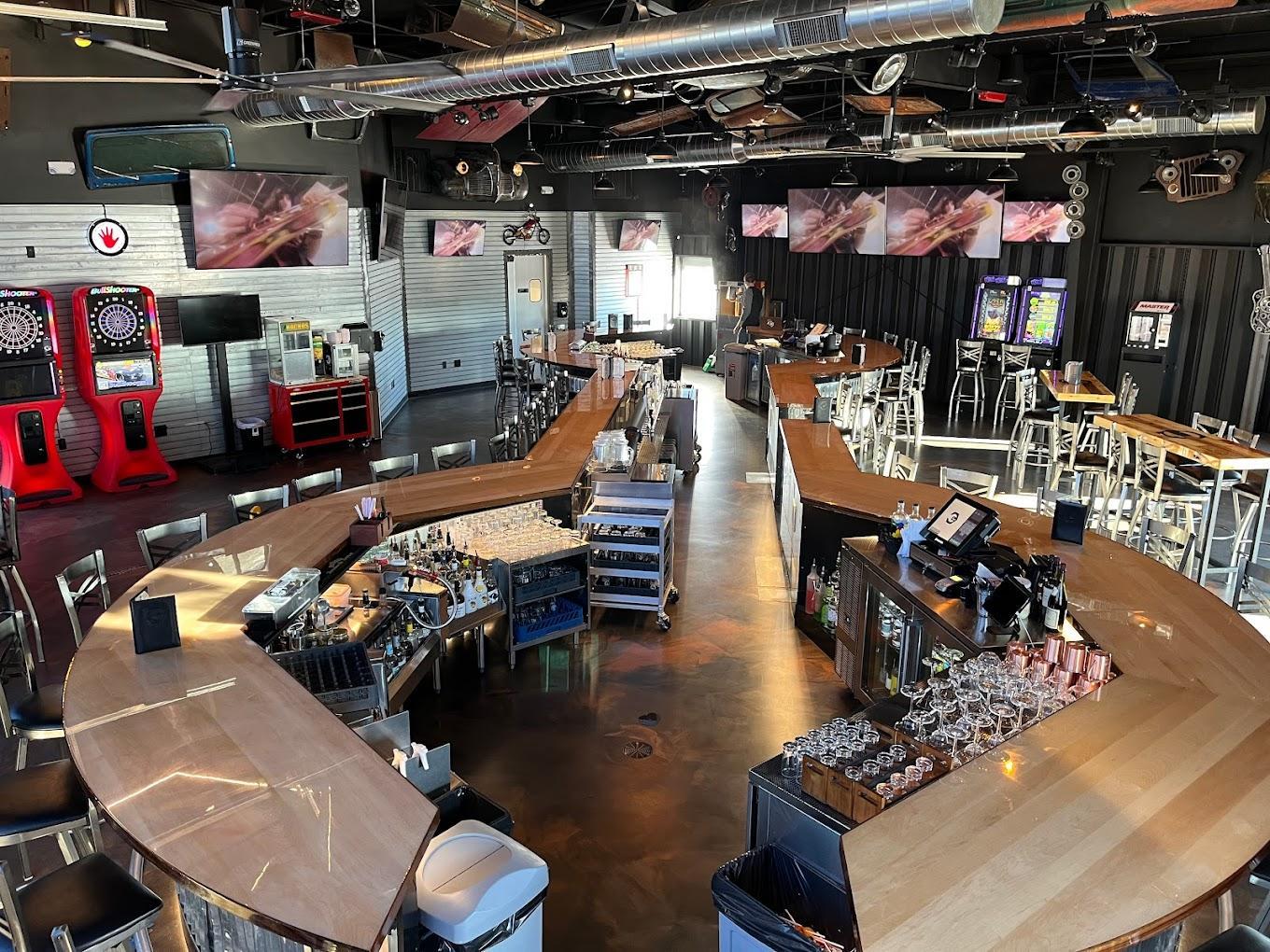 Spacious modern bar with wooden counters and steel chairs, featuring arcade games.
