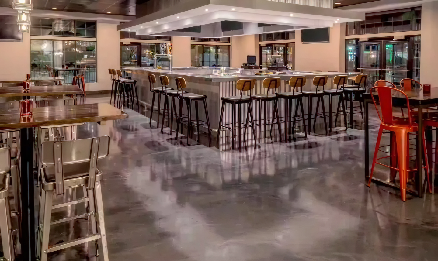 Bar with tall chairs around a central island, polished floor, modern decor.