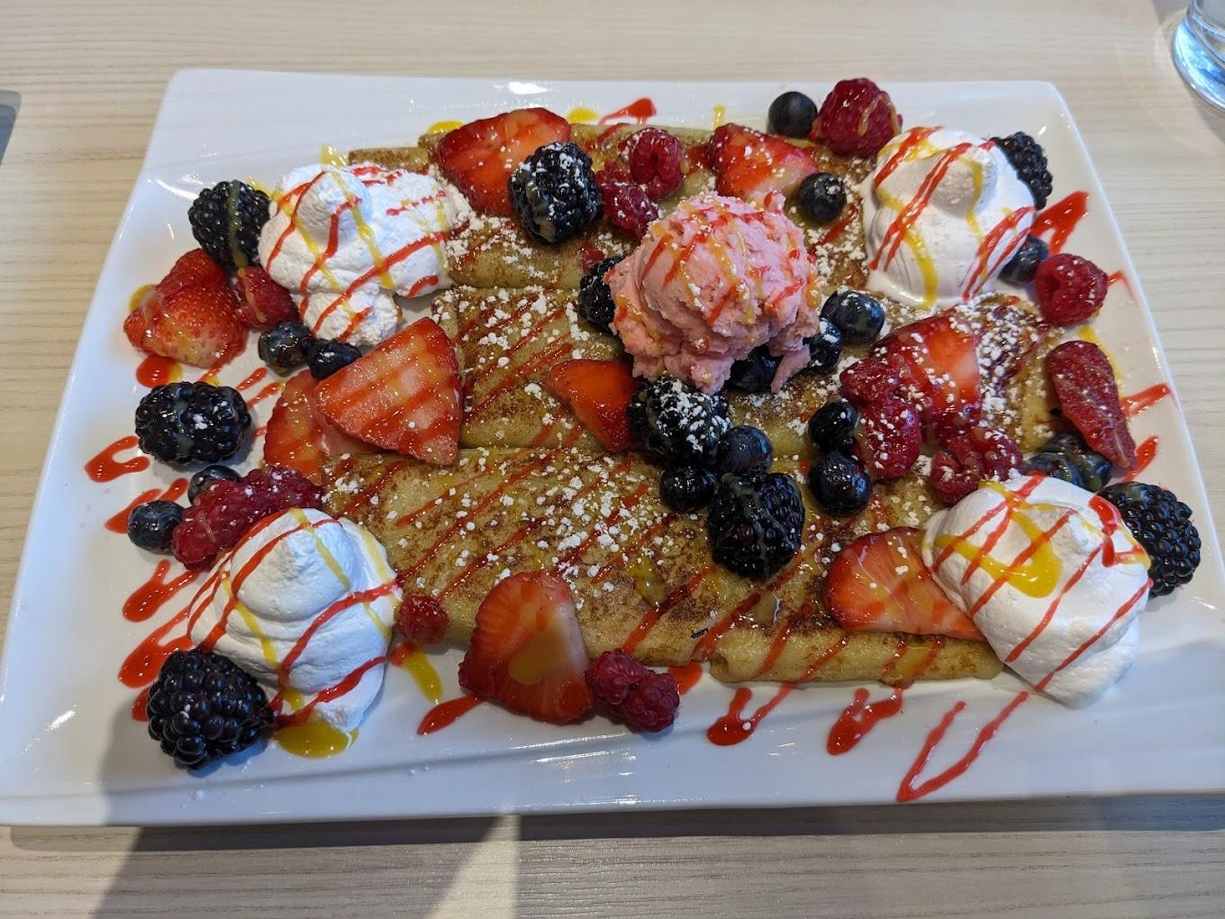 Waffles topped with berries, whipped cream, and syrup on a white plate.