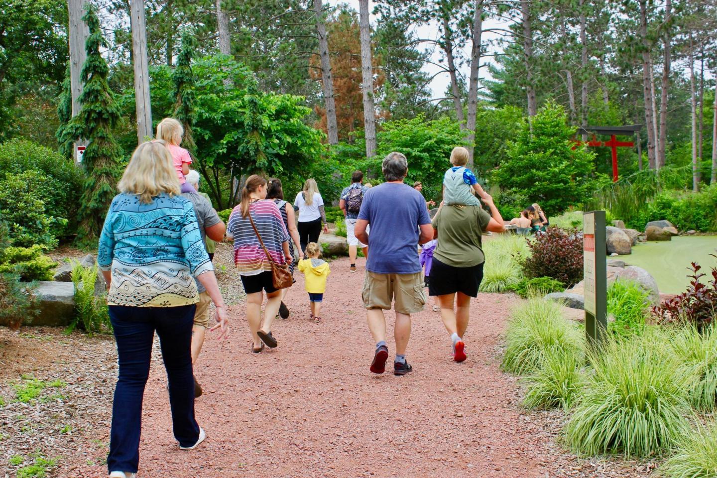People walking on a garden path surrounded by trees and greenery.