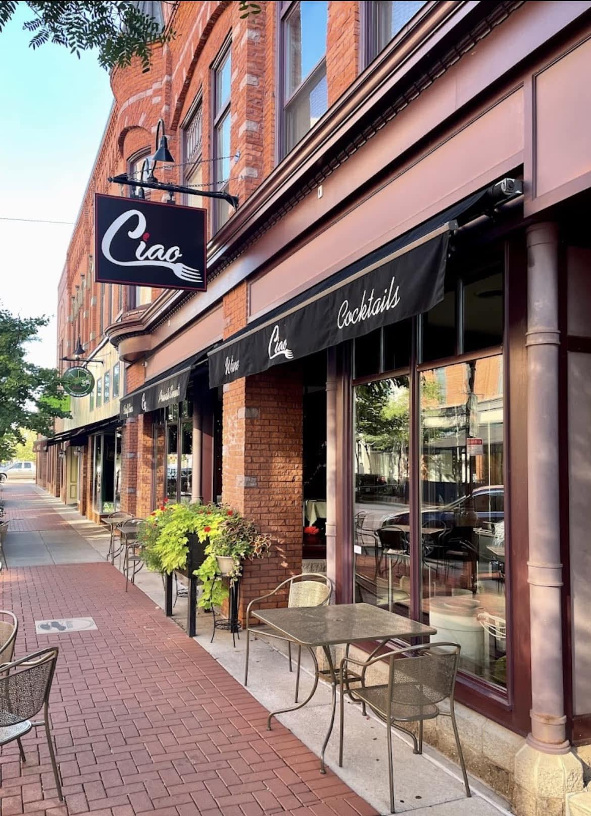 Brick sidewalk outside a cafe with outdoor seating and a black awning.