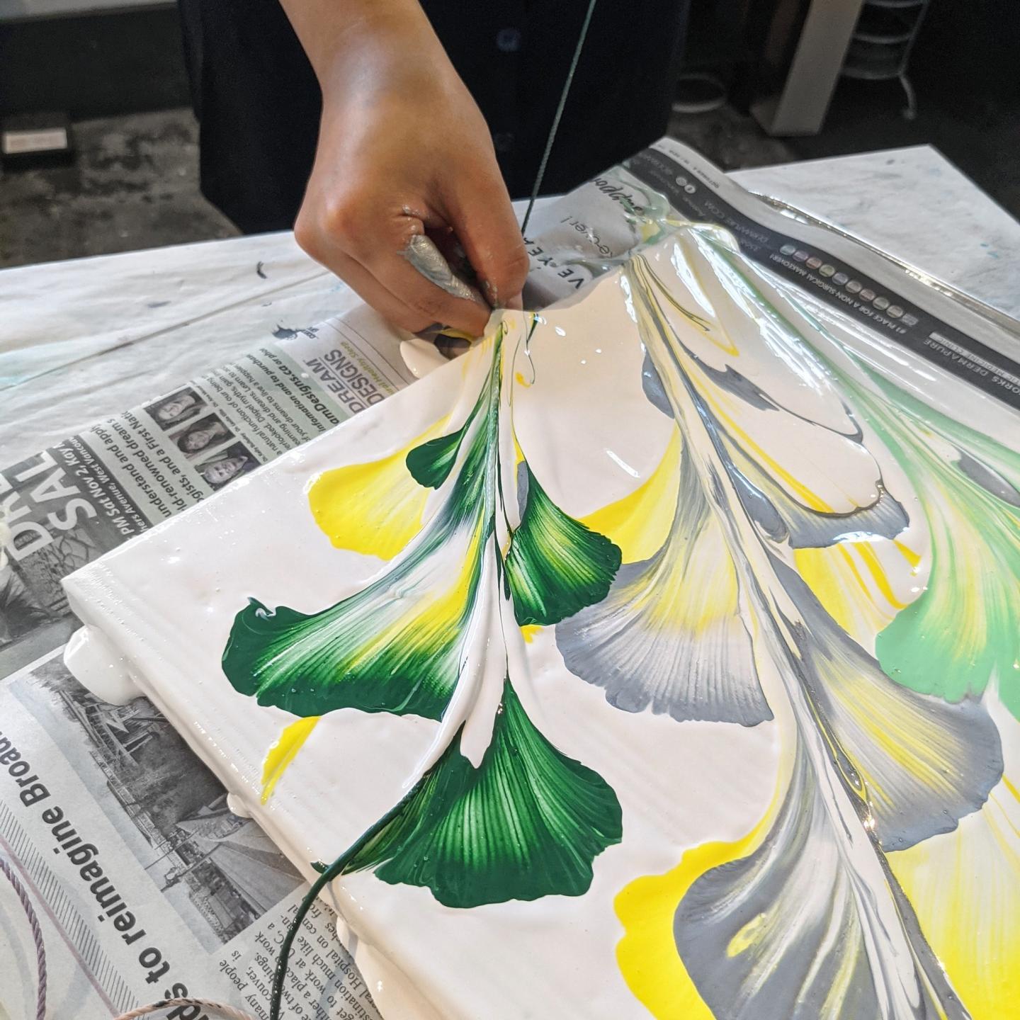 Hand creating abstract floral art with green and yellow paint on a white canvas.
