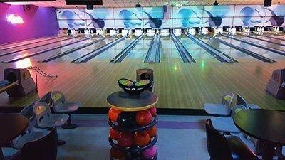 Bowling alley with stacked colorful balls and empty lanes, lit by neon lights.