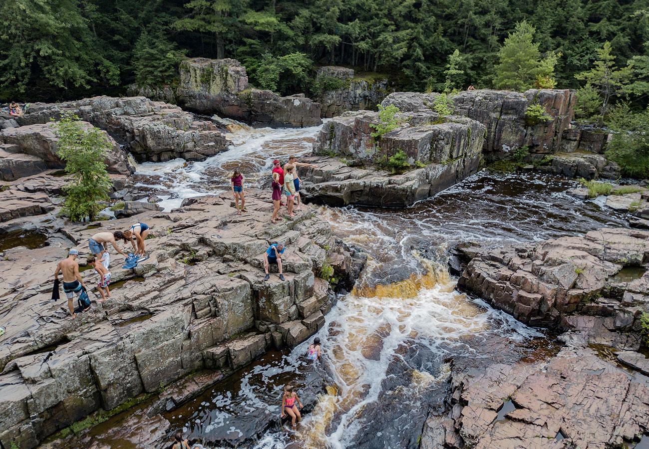 People exploring rocky waterfall surrounded by forest.