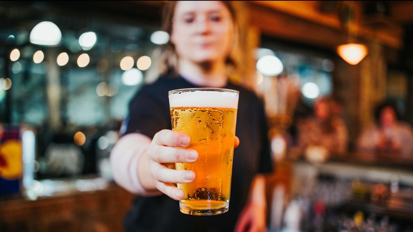 Person holding a glass of beer in a bar setting.