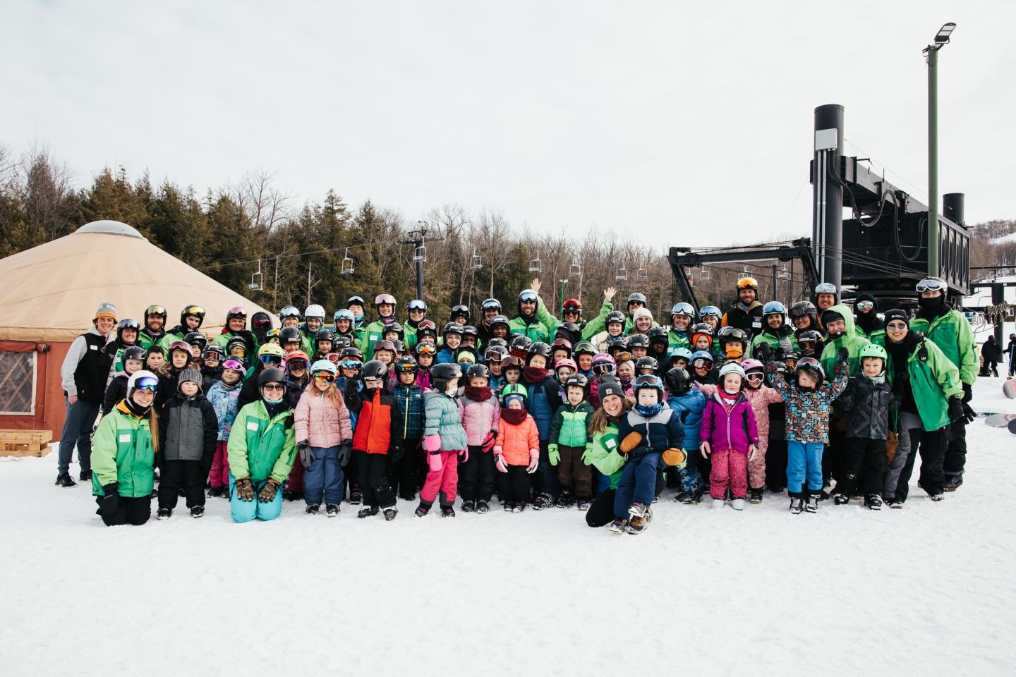 Large group of people in winter gear posing on a snowy backdrop.