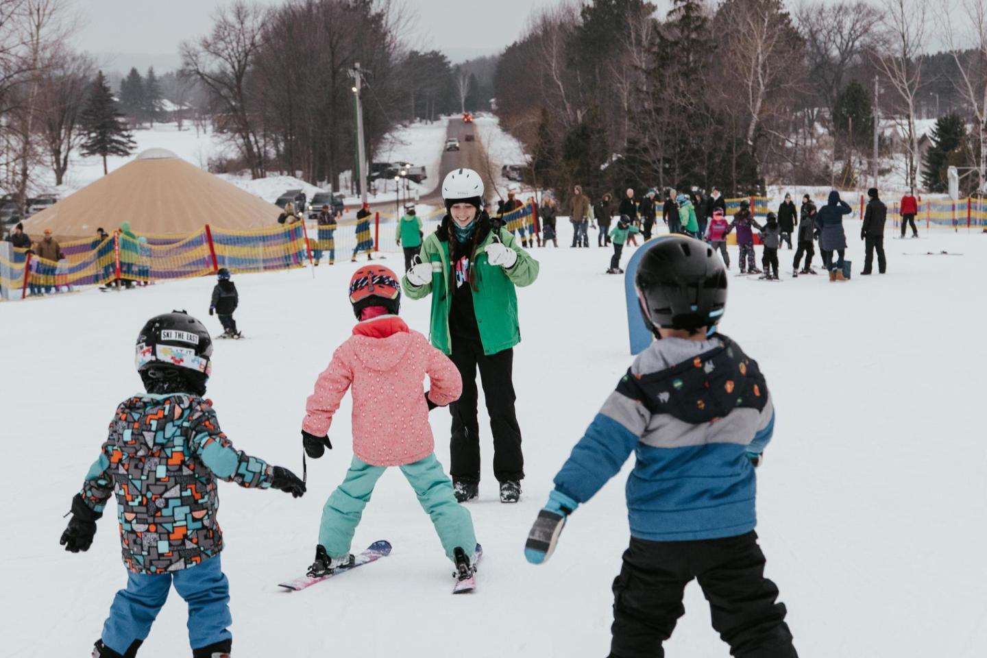 Children in colorful gear learning to ski on a snowy slope.