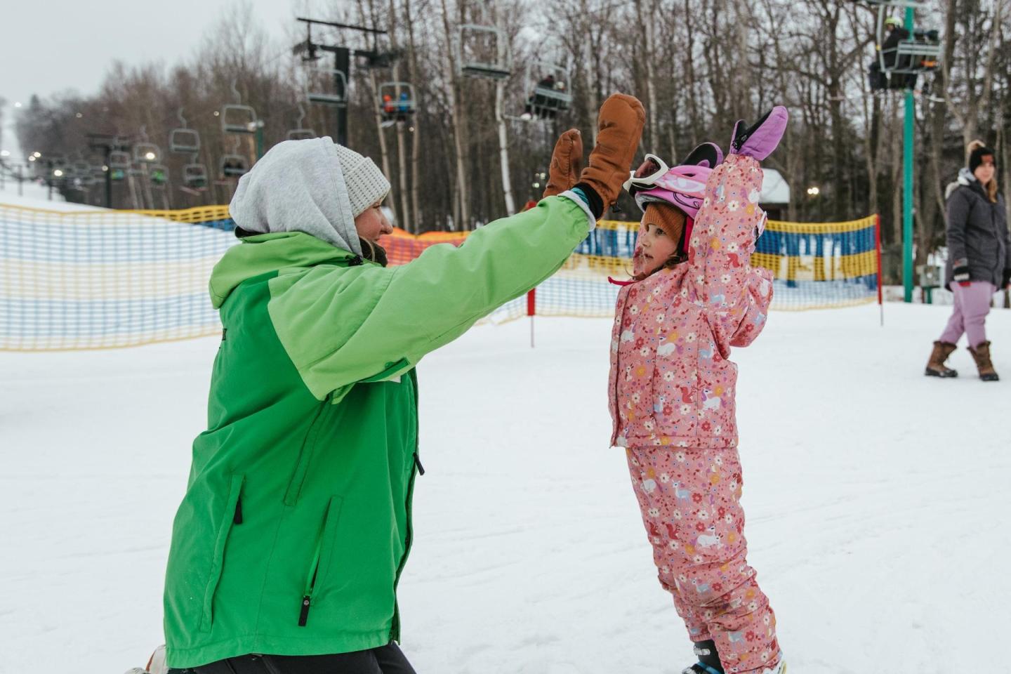 Adult and child high-five on a snowy ski slope.