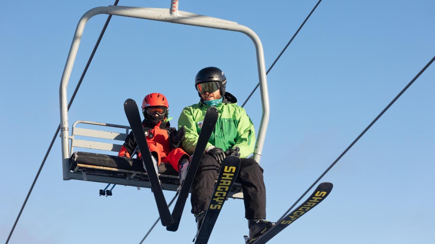 Skiers on a chairlift in colorful gear under a clear blue sky.