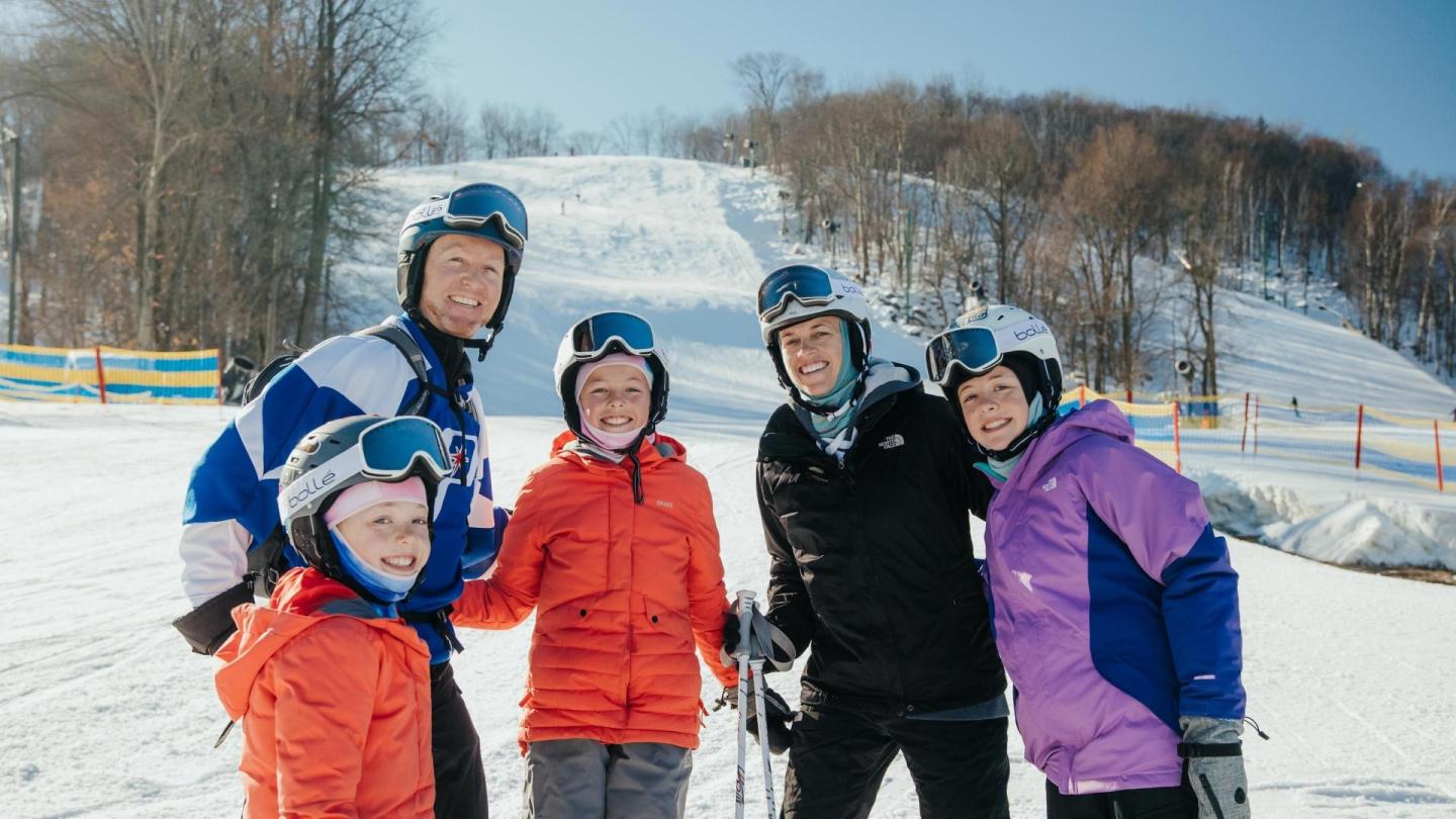Family in ski gear smiles on snowy slope.