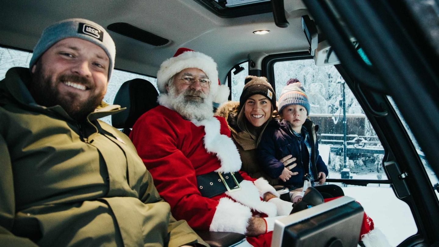 Group of people in winter clothes smiling in a vehicle, with one dressed as Santa Claus.