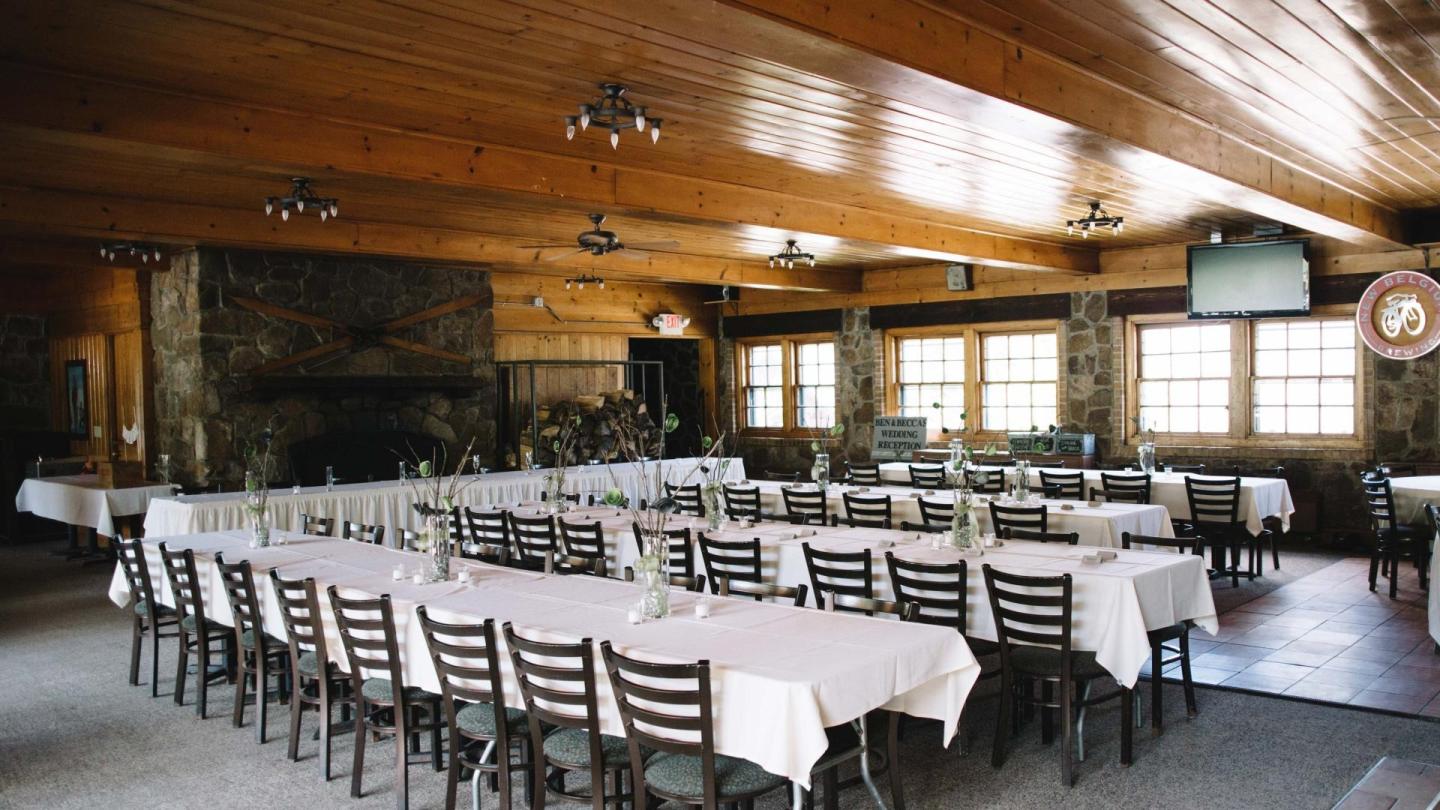 Rustic dining room with white tablecloths, wooden ceiling, and large windows.