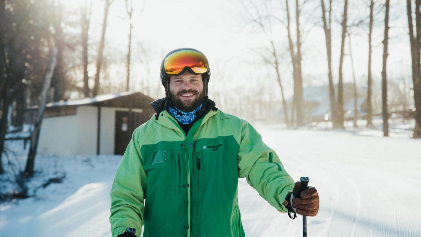 Person skiing in bright green jacket, snow-covered path, sunny winter day.