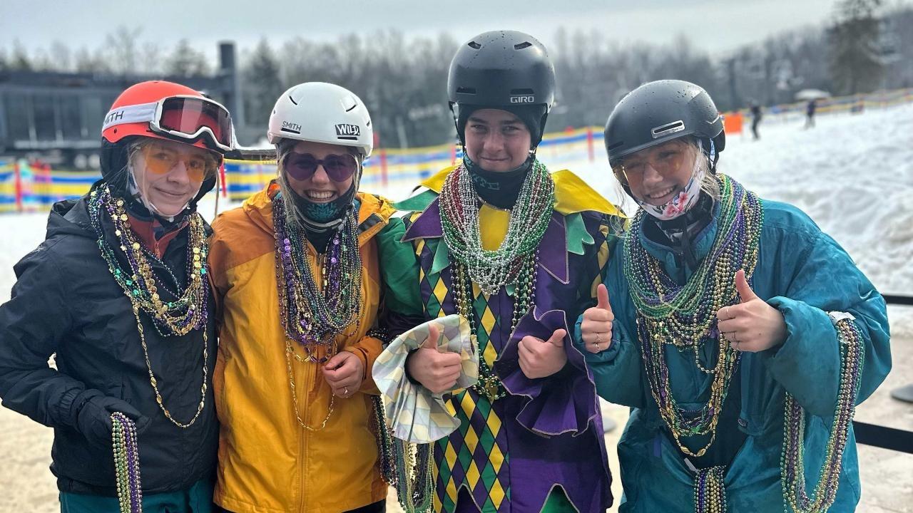 Four people in winter gear with beaded necklaces, smiling on a snowy day.