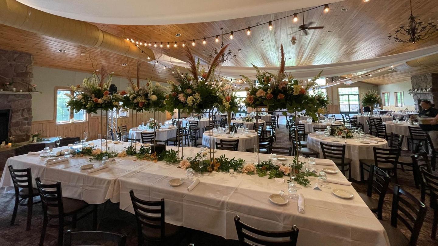 Elegant dining room with white tablecloths, floral centerpieces, and string lights.
