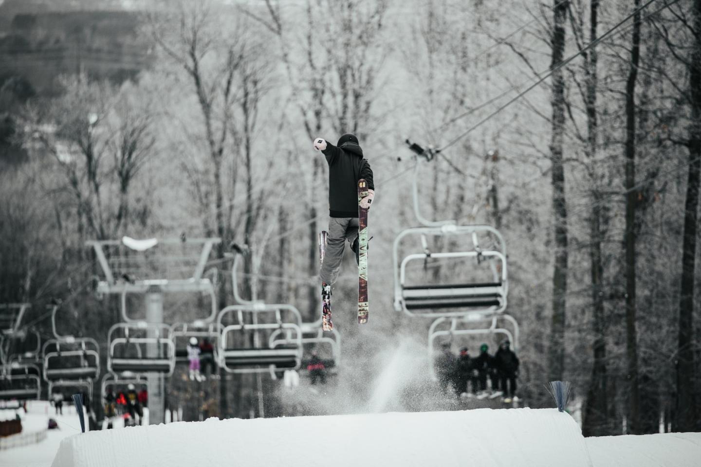 Snowboarder jumping near ski lifts in a snowy forest.