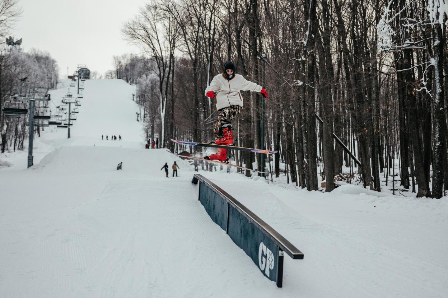 Snowboarder jumping off a rail in a snowy forested area.