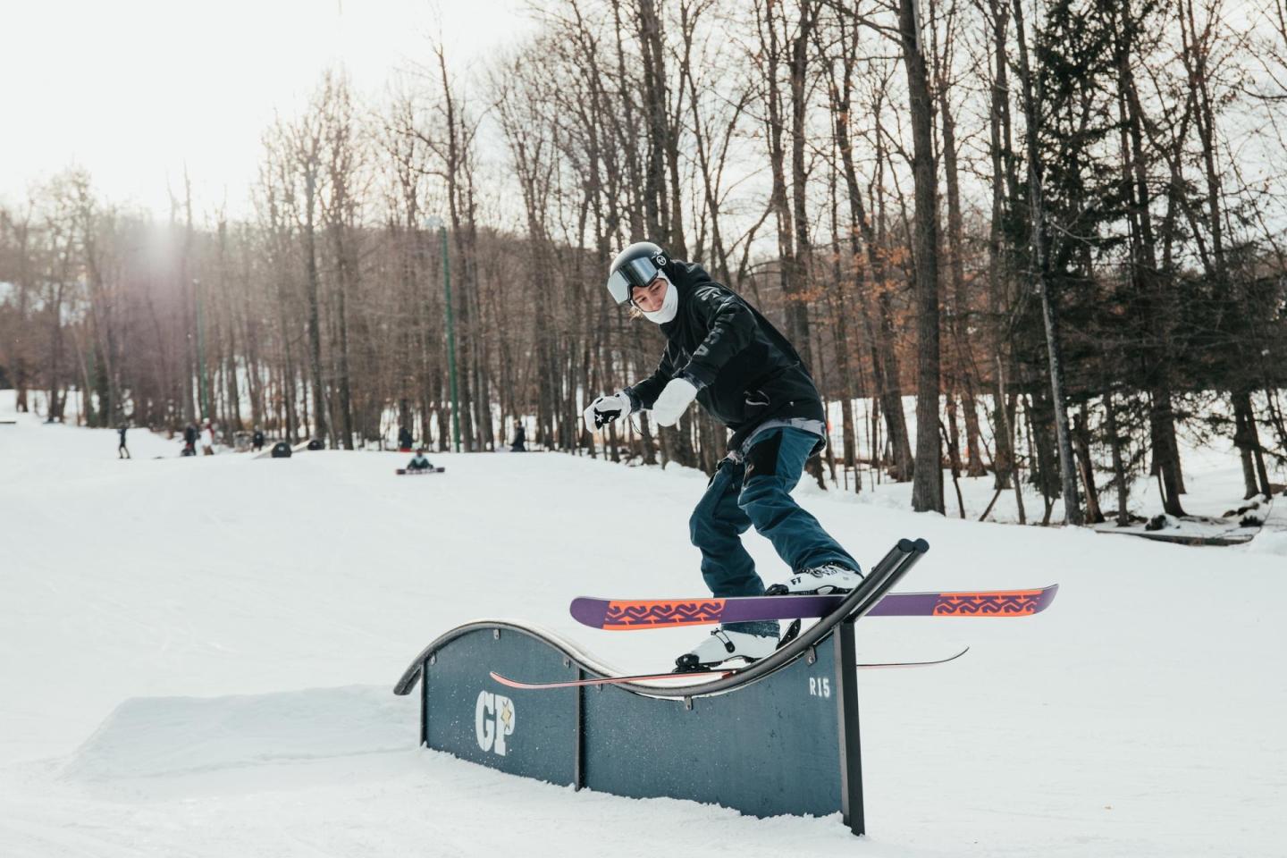 Snowboarder performing a trick on a snowy rail in a forested area.