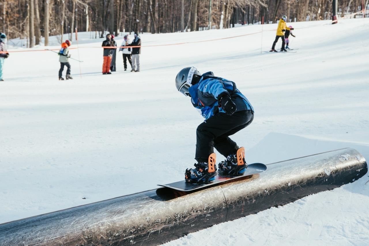 Snowboarder in blue jacket sliding on a rail in a snowy park.