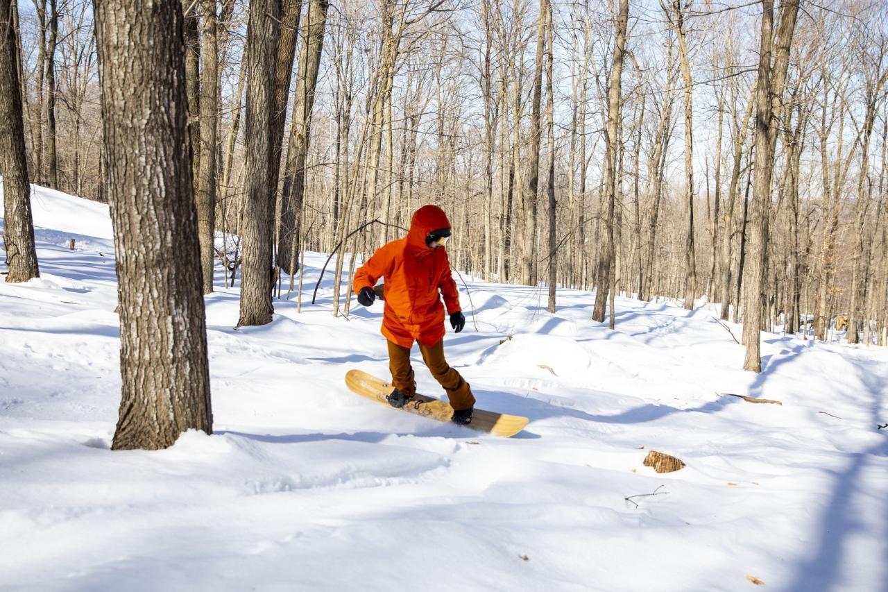 Snowboarder in orange gear gliding through snowy forest.